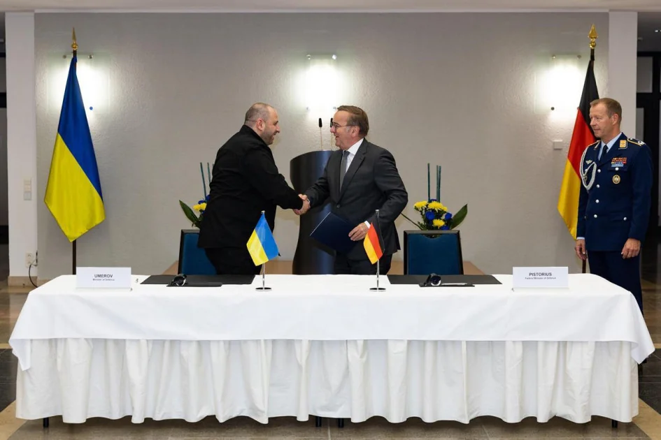 Рукостискання представників України та Німеччини під прапорами країн за столом переговорів