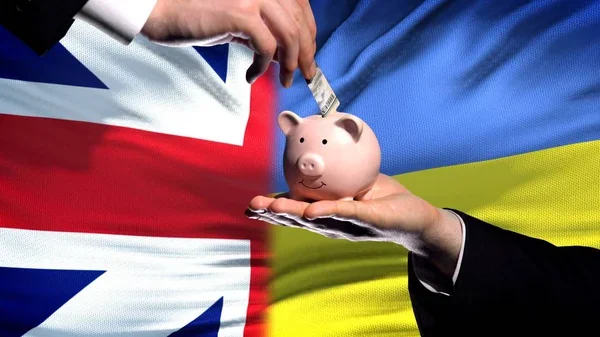 Велика Британія передає $1 млрд Україні: рука вкладає гроші в скарбничку на тлі прапорів