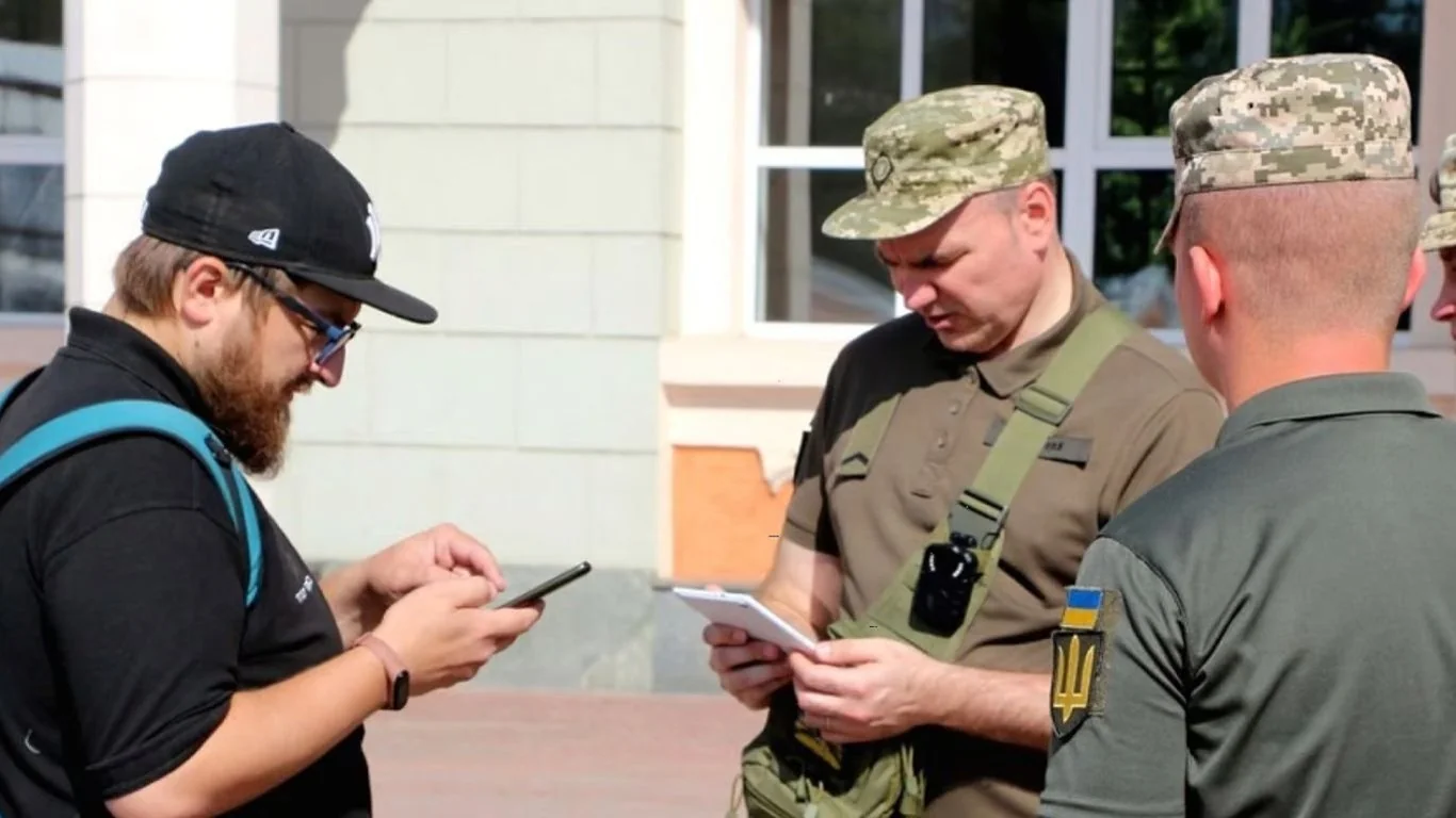 Співробітники ТЦК перевіряють телефон бородатого чоловіка на вулиці