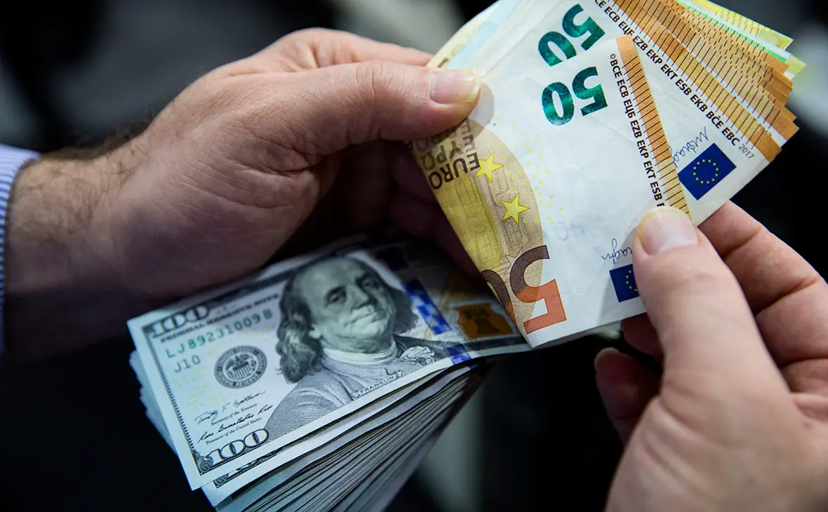Пачки доларів і євро в руках на тлі курсу валют в Україні