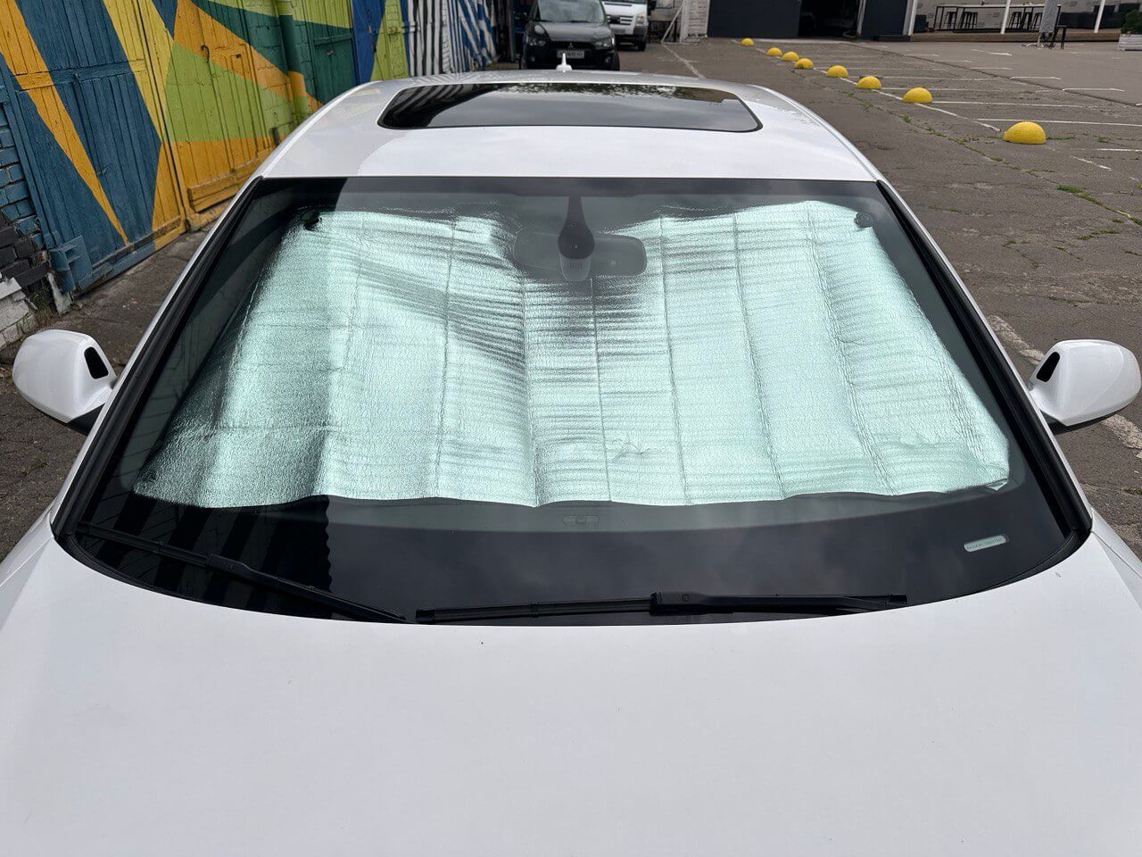 Білий автомобіль із сонцезахисною шторкою на лобовому склі для охолодження салону