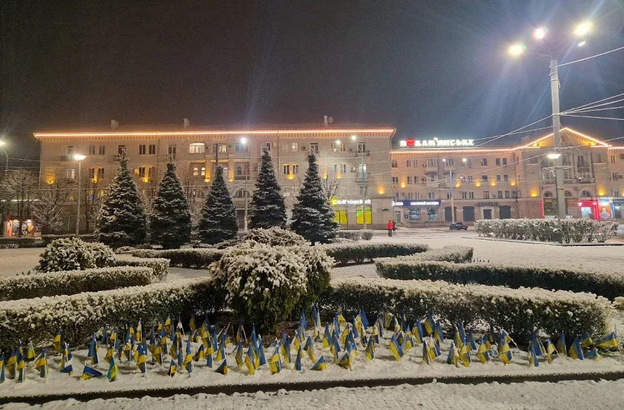 Засніжена площа з українськими прапорами вночі під час похолодання