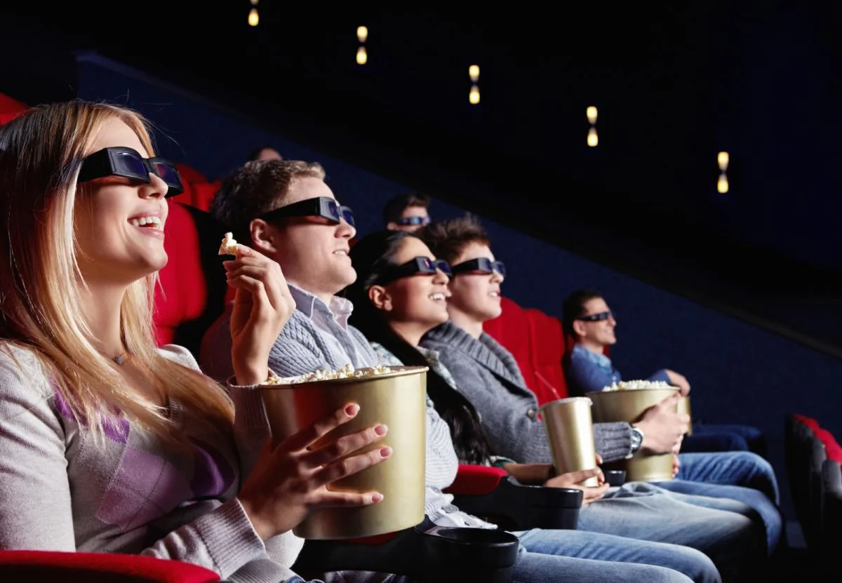 Молоді люди в кінотеатрі з 3D-окулярами та попкорном