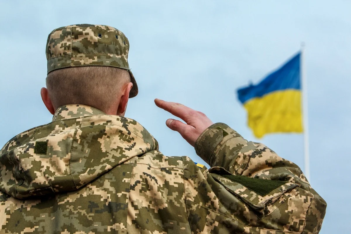 Військовослужбовець ЗСУ салютує прапору України під час воєнного стану