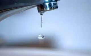 З хромованого крана звисає і падає крапля води на розмитому тлі