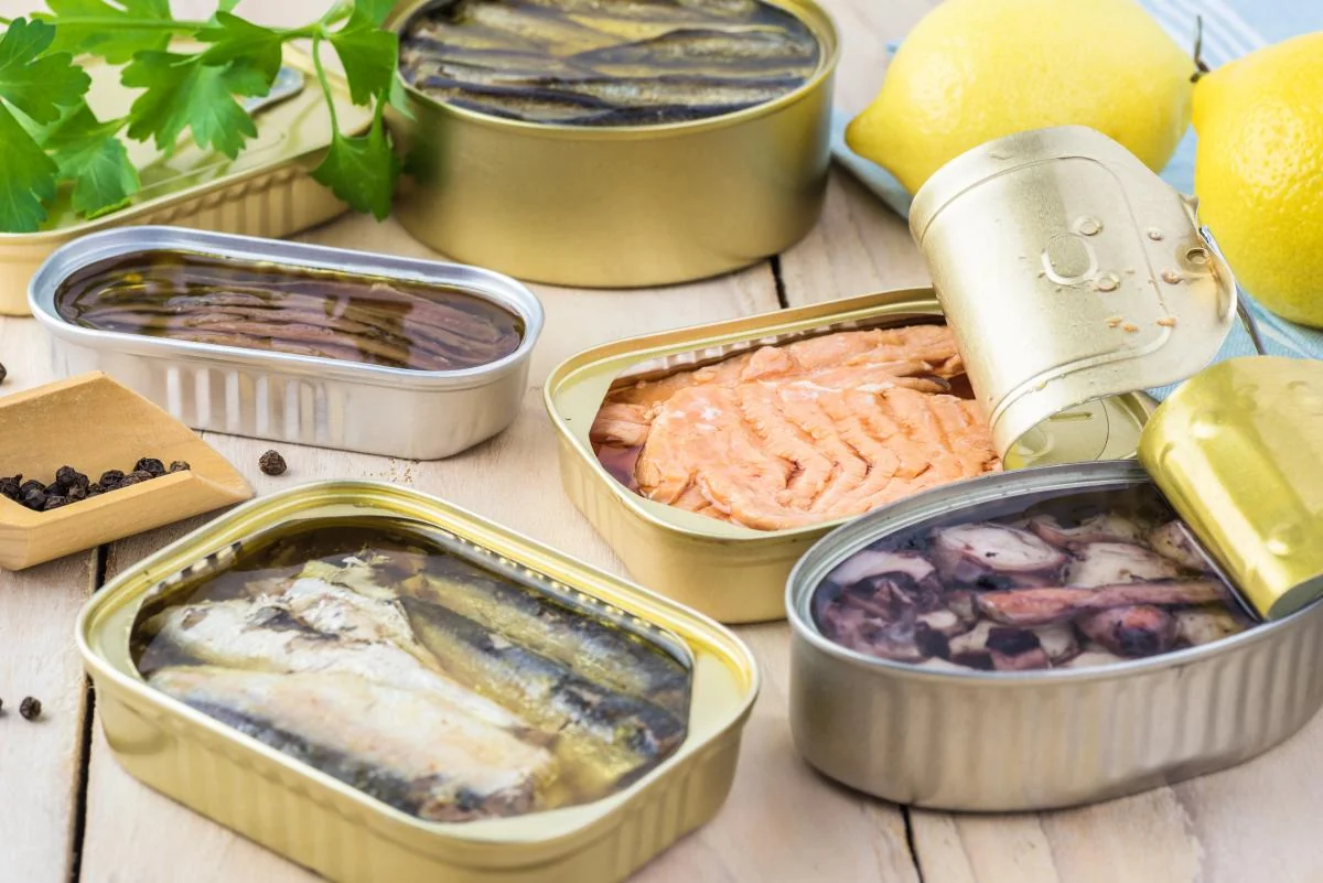 Відкриті консерви з сардинами, лососем і морепродуктами, лимони та петрушка на столі