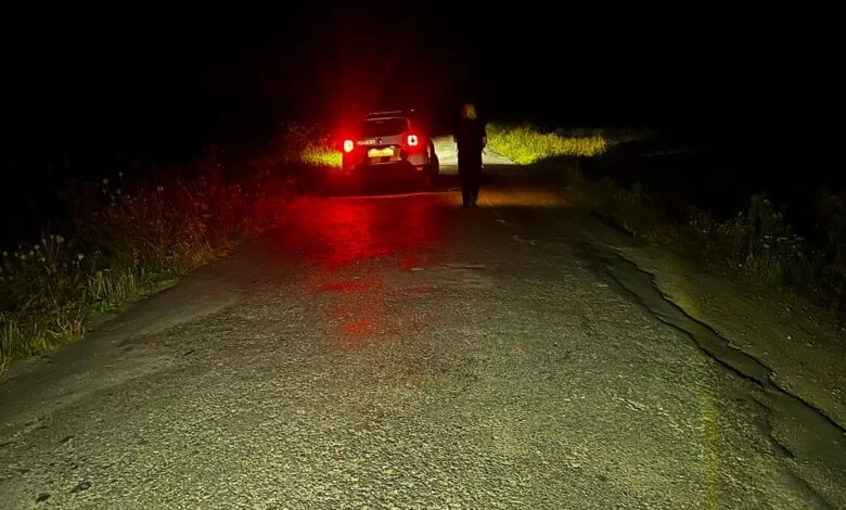Автомобіль із червоними стоп-сигналами та силует людини на сільській дорозі вночі