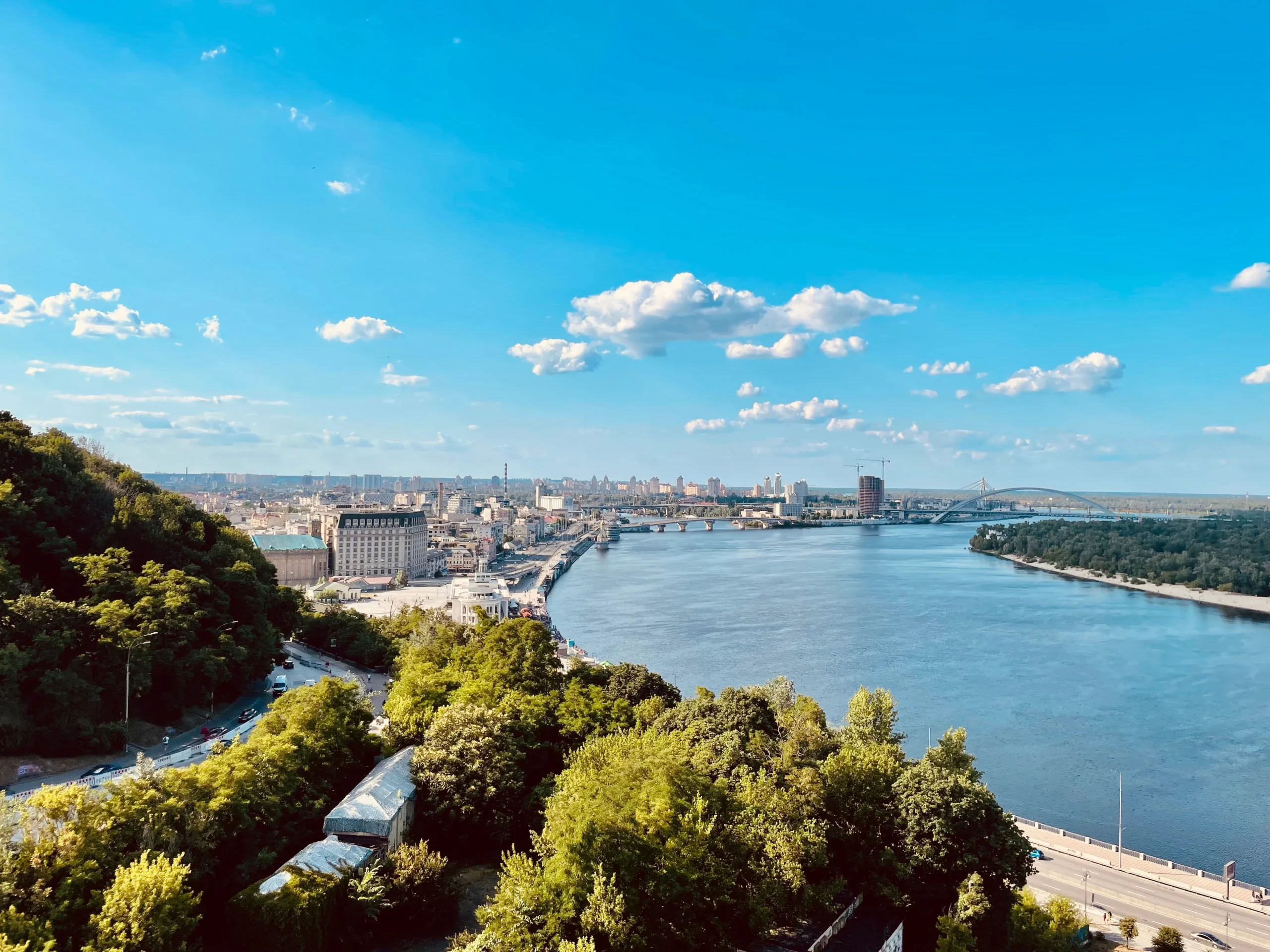 Панорама Києва з Дніпром, мостами та зеленими схилами під ясним небом