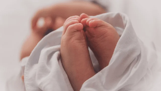 Крупний план ніжок новонародженого малюка, загорнутих у білу пелюшку