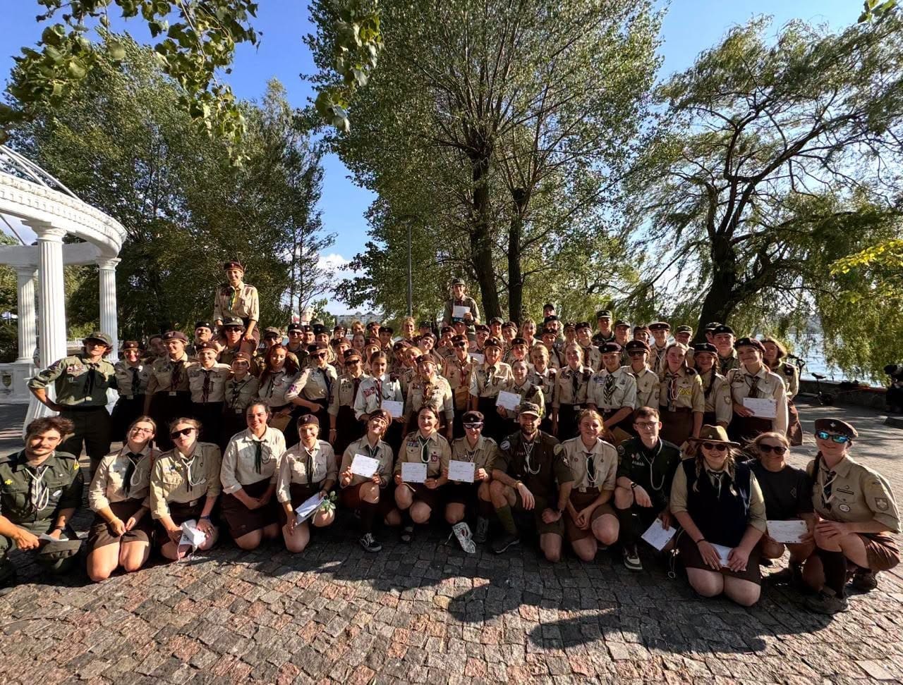 Велика група пластунів у одностроях позує біля альтанки та дерев